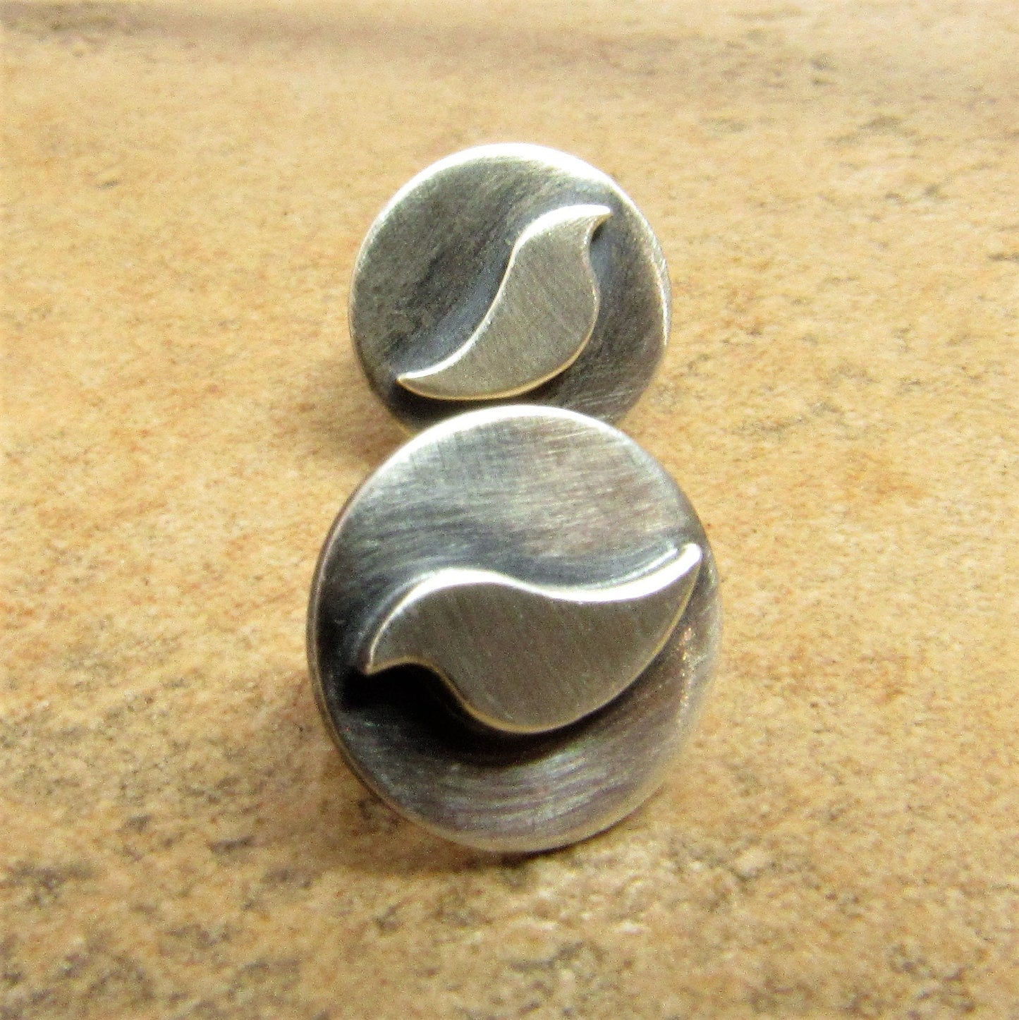 Pair of silver disk post back earrings with bird design on a beige background