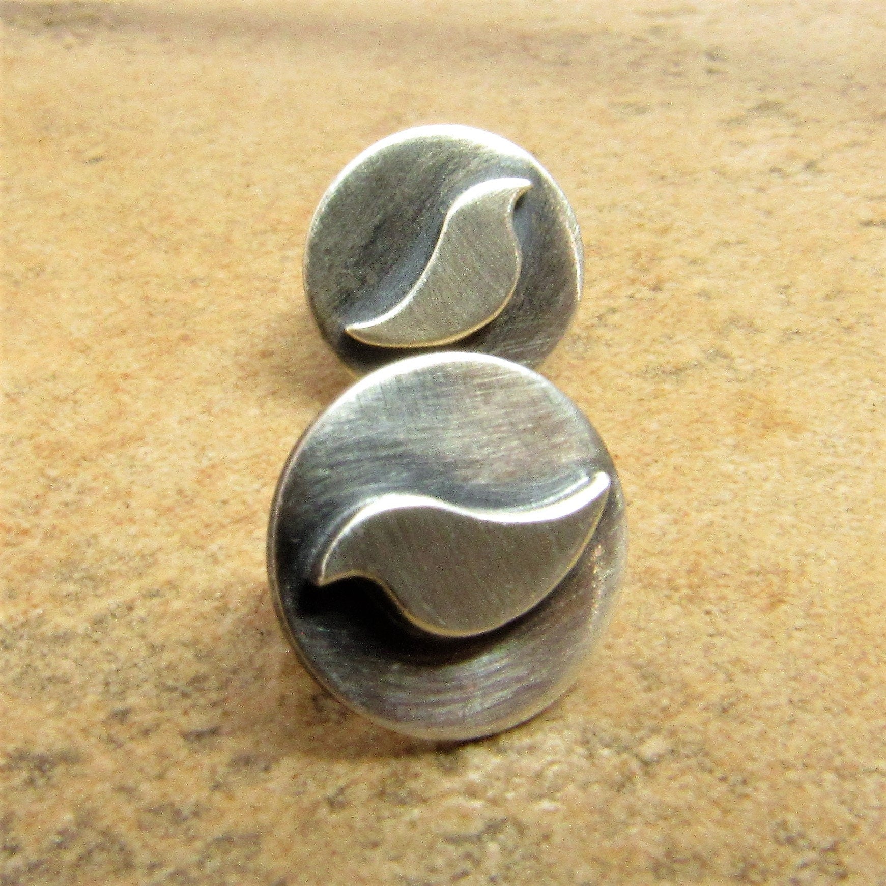 Pair of silver disk post back earrings with bird design on a beige background