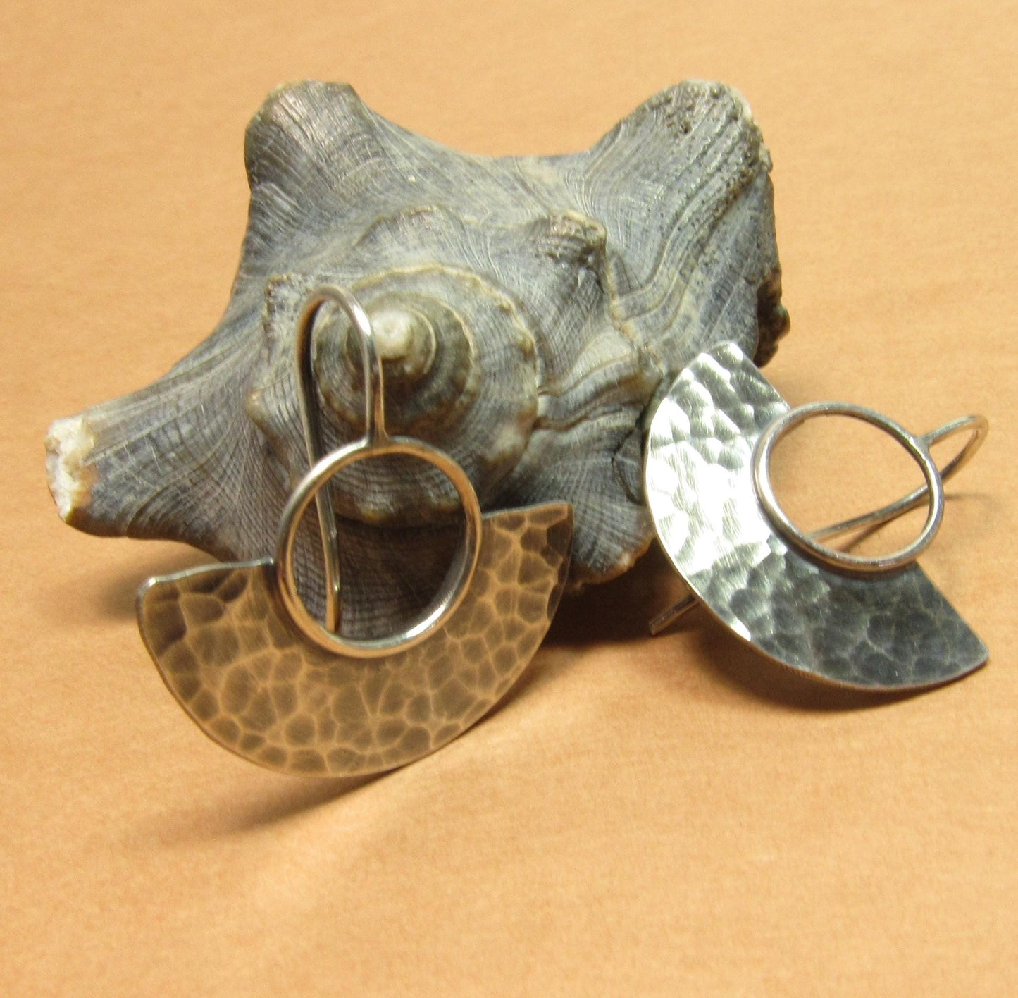 Pair of silver fan earrings with textured designs on a shell against orange background.