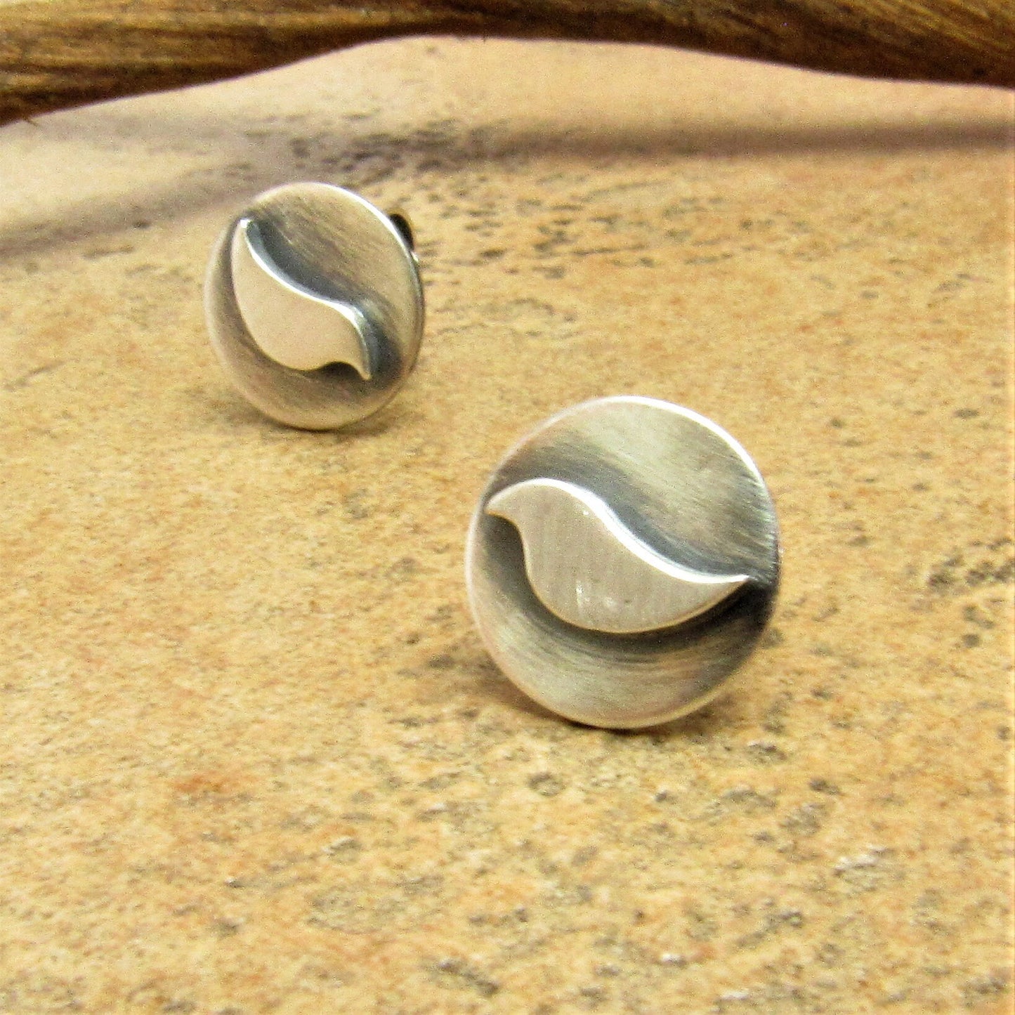 Handmade sterling silver bird studs with oxidized finish, lightweight everyday earrings for nature lovers. Photo against driftwood and stone surface