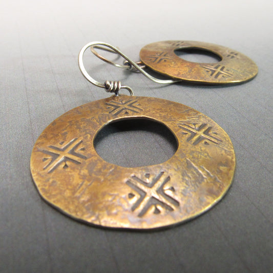 Pair of bronze coin style earrings with circular design on a gray background