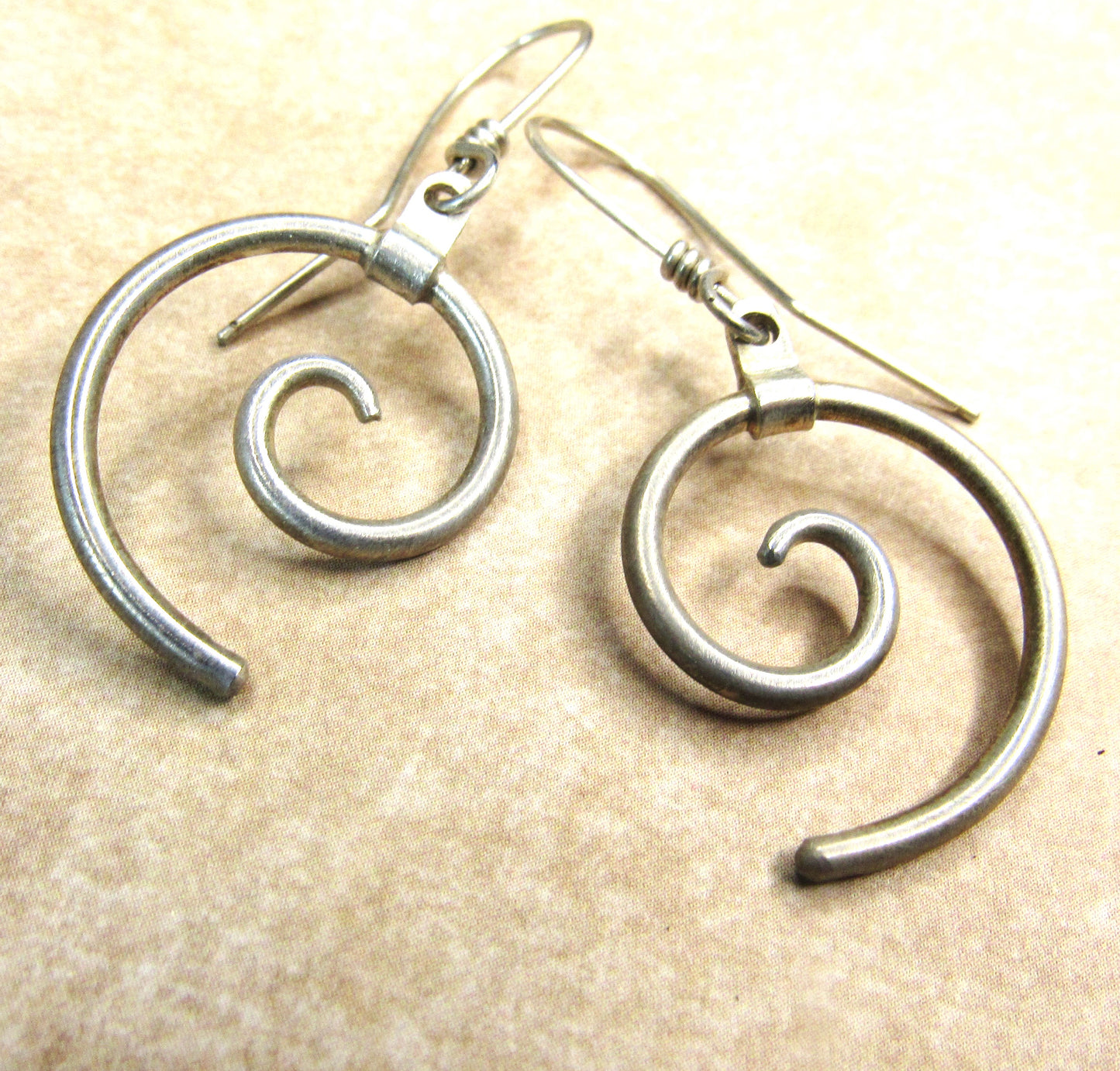 Pair of argentium silver spiral earrings on a beige background