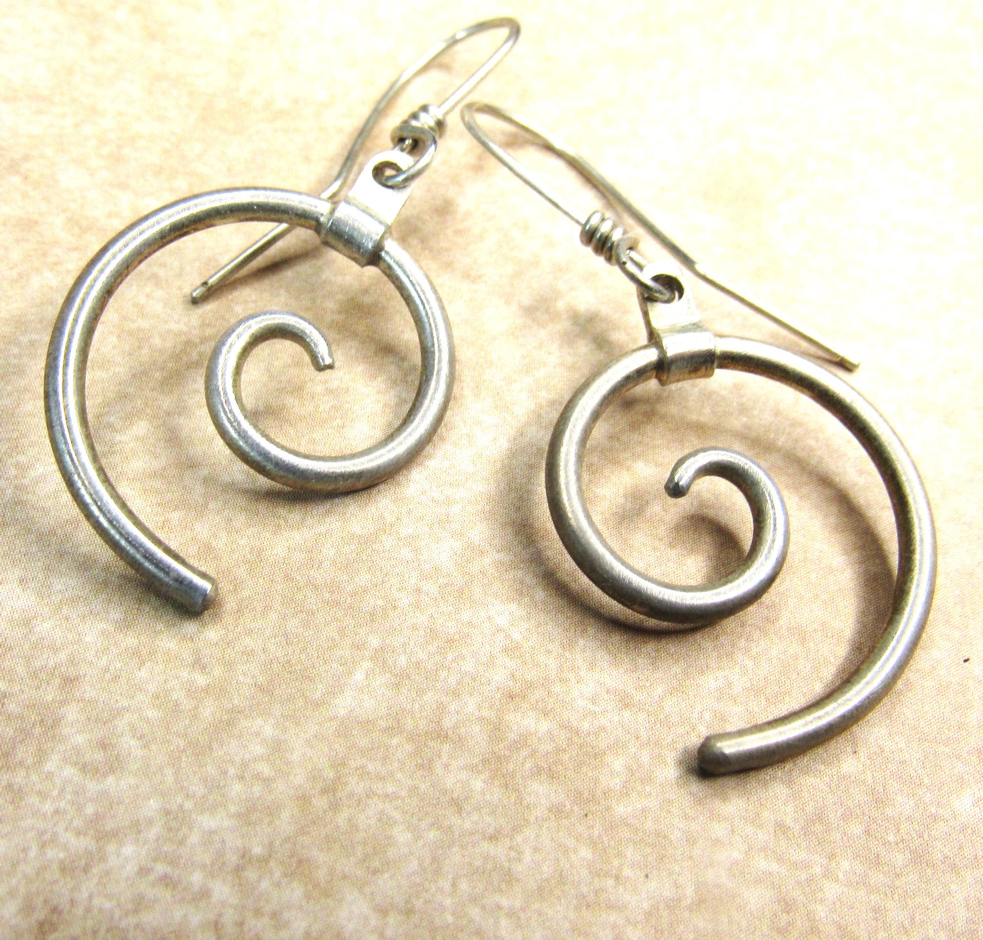 Pair of argentium silver spiral earrings on a beige background