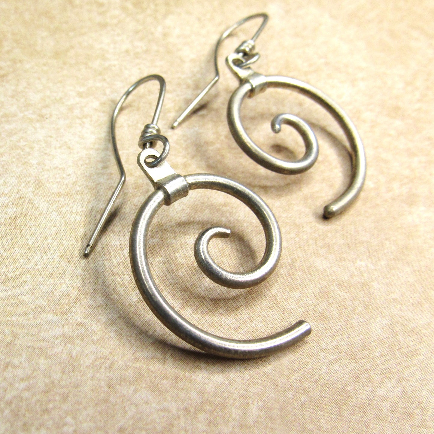 Silver spiral earrings on a beige background showing wrapped ear wires and smooth finish.