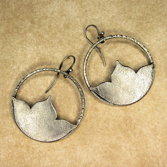 Pair of large silver hoop earrings with lotus shape on a beige background.
