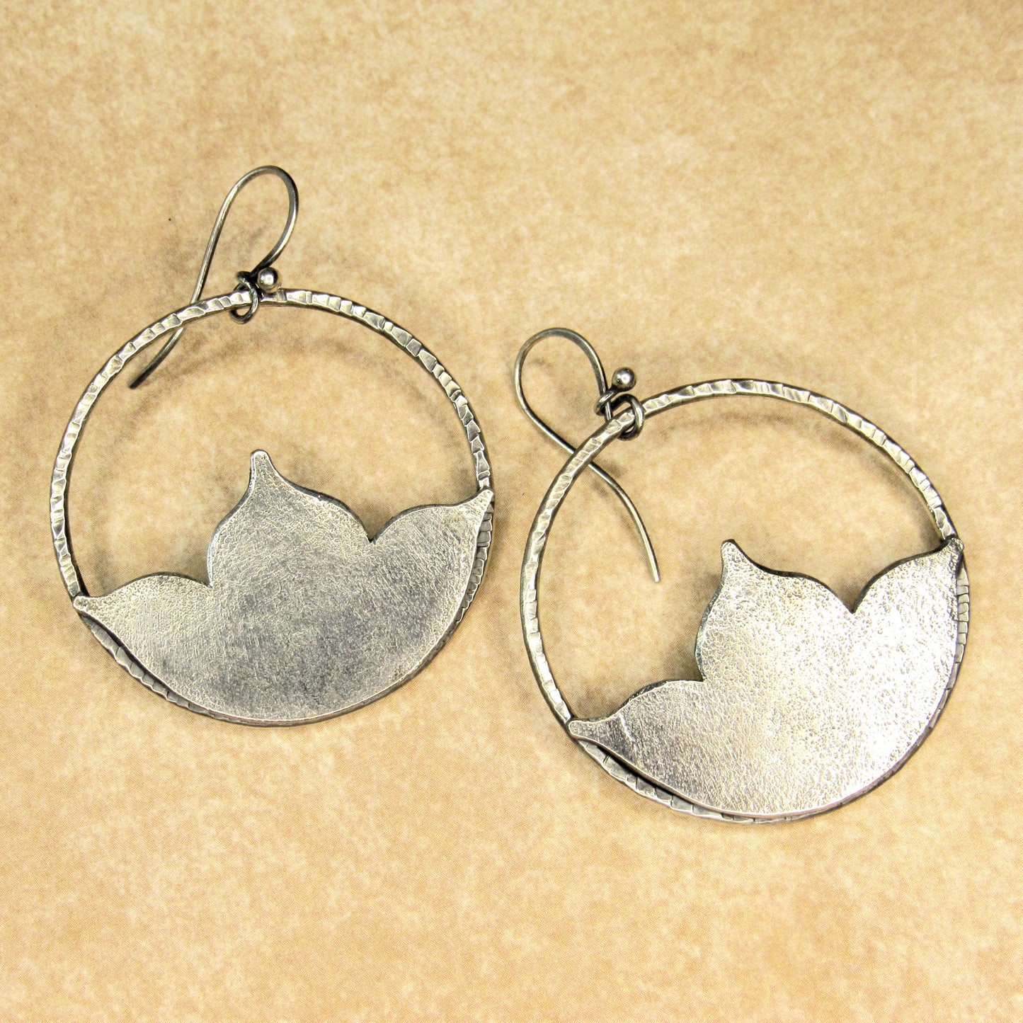 Large silver lotus hoop earrings  on a beige background.