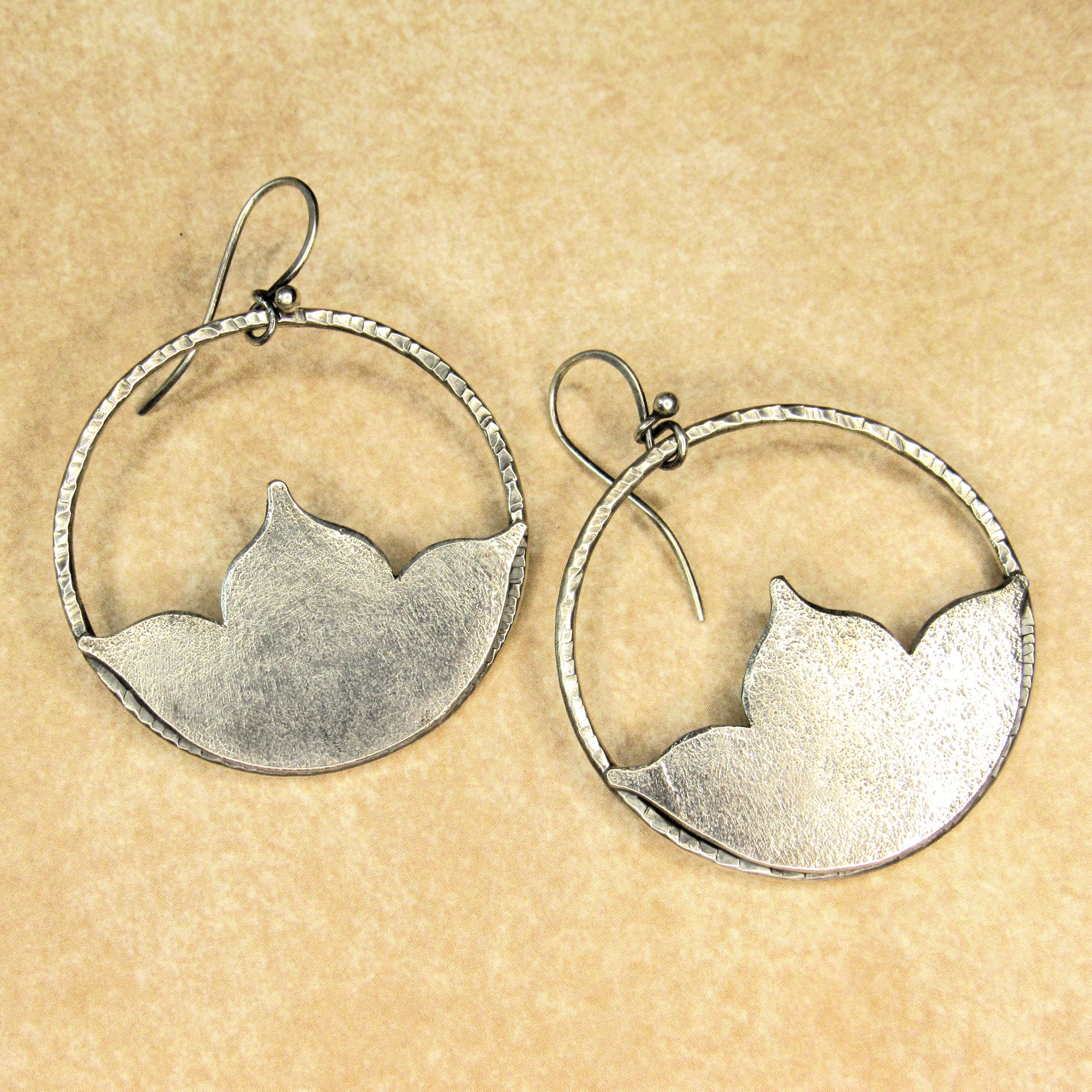 Large silver lotus hoop earrings  on a beige background.