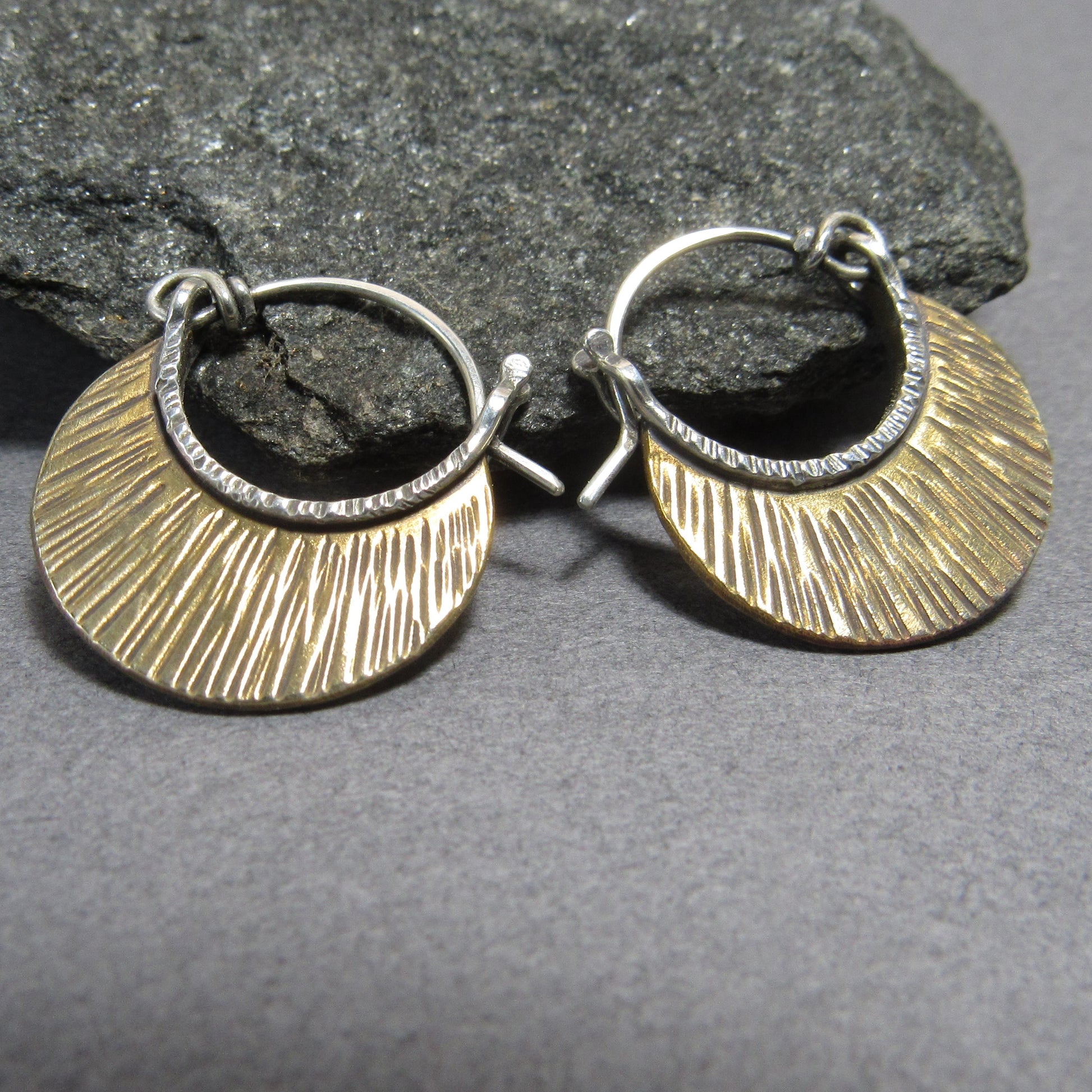 Pair of  small mixed metal bronze and silver hoop earrings on a gray surface