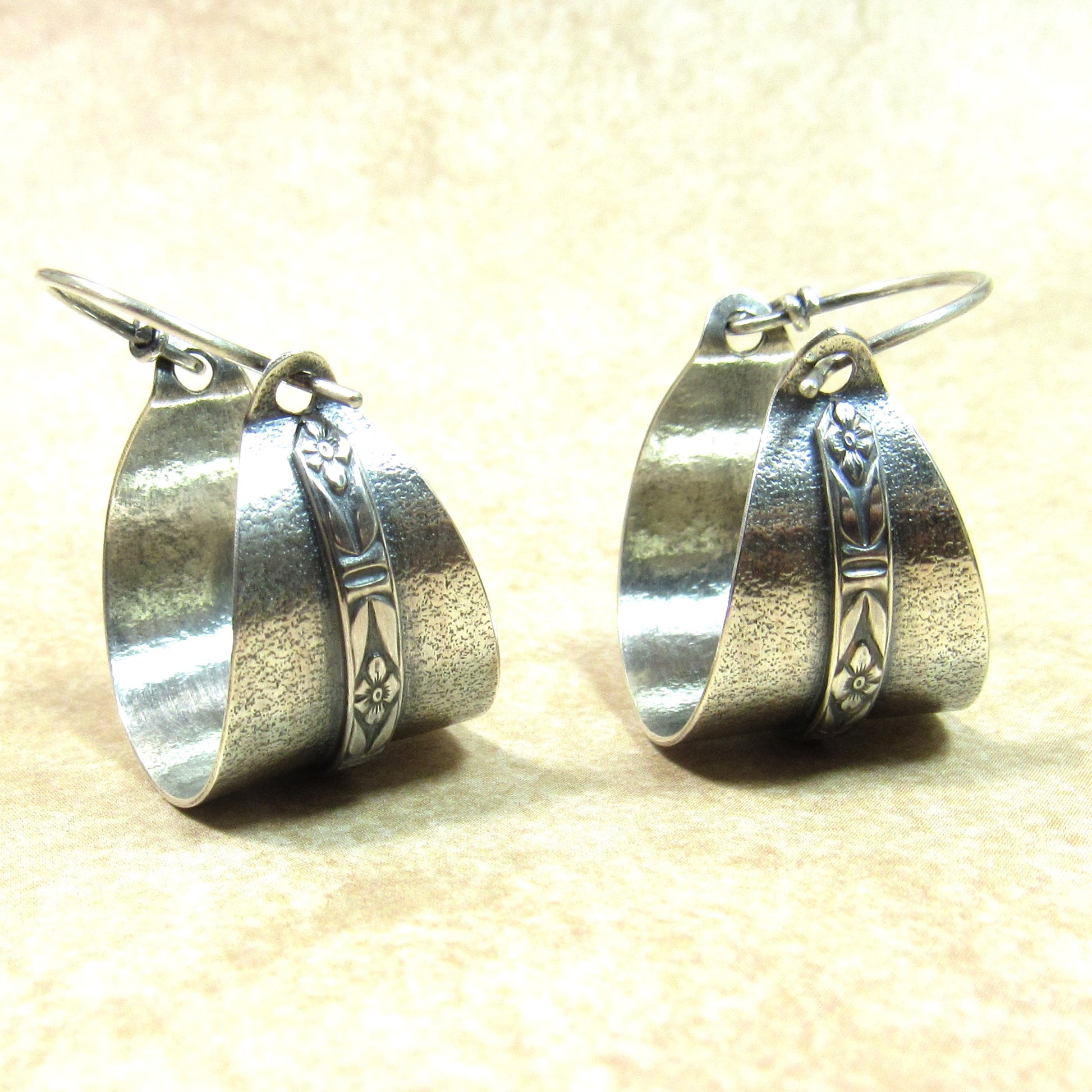 Pair of everyday argentium basket style silver hoop earrings on a beige background.