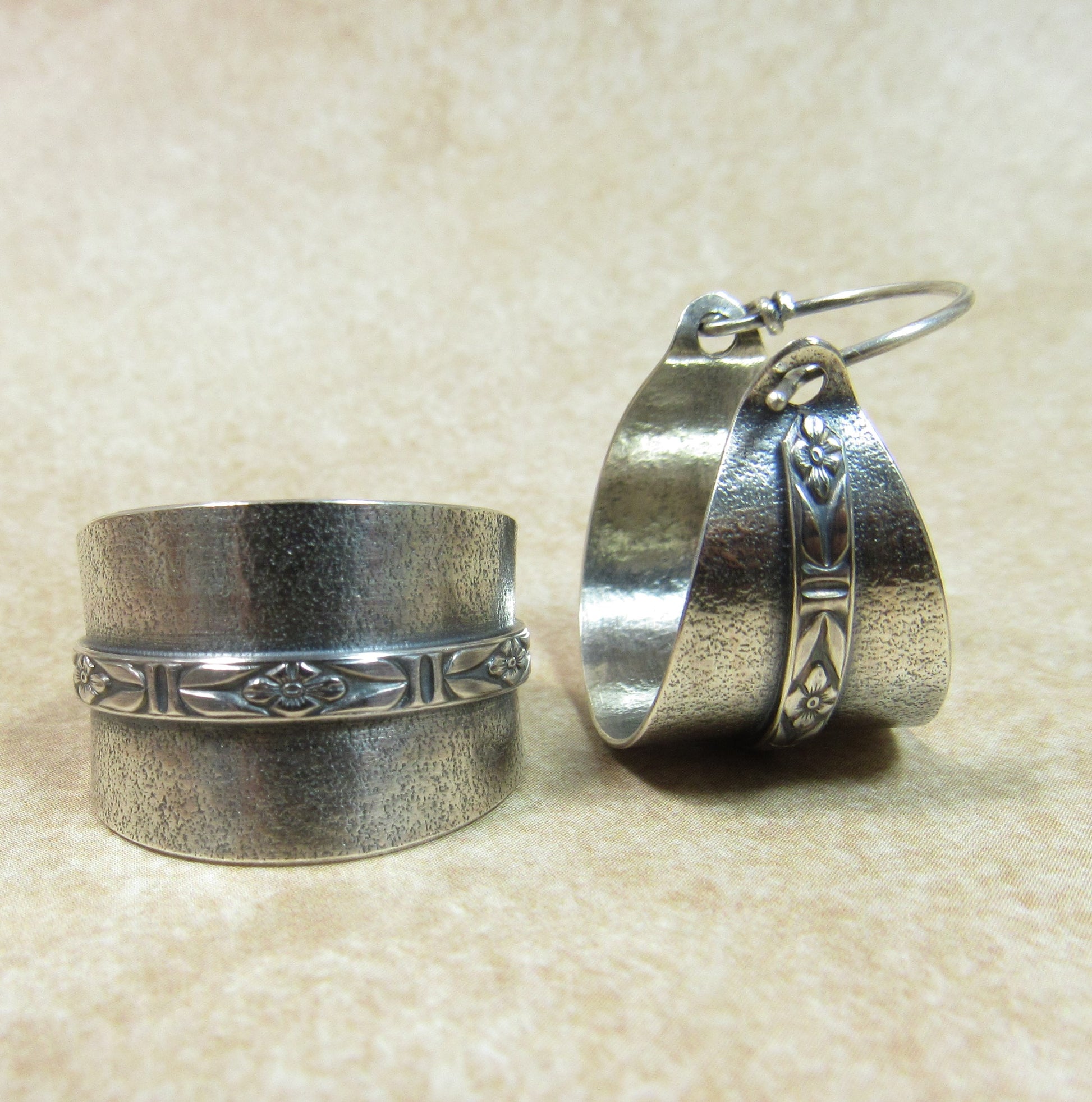 Argentium silver hoop earrings with floral designs on a beige background showing side view and laying flat.
