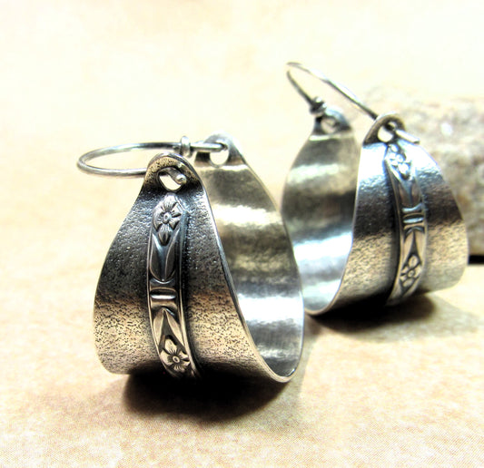 Pair of silver hoop earrings by mocahete with floral designs on a beige background.