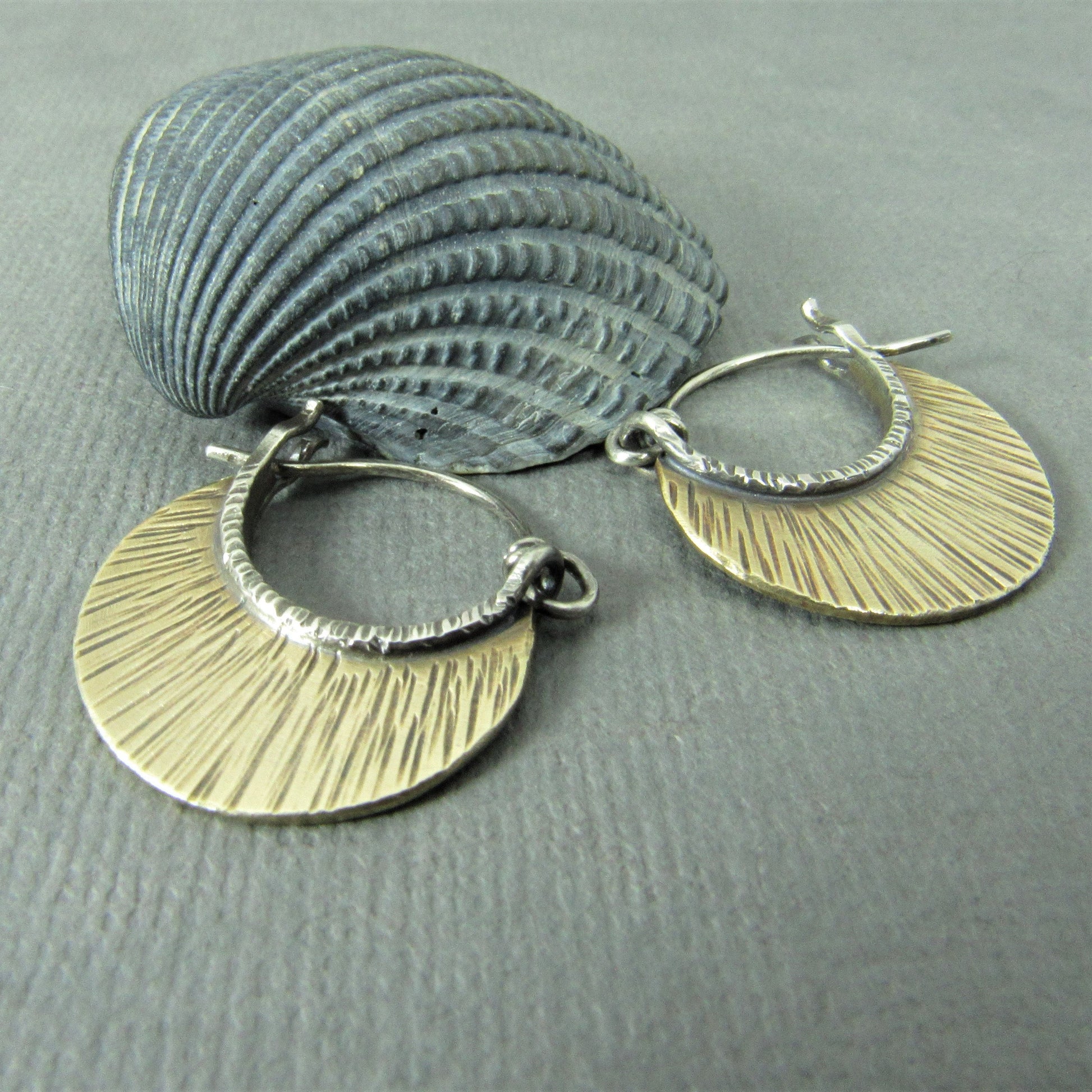 Pair of small silver and bronze hoop earrings on a textured gray surface with a shell.
