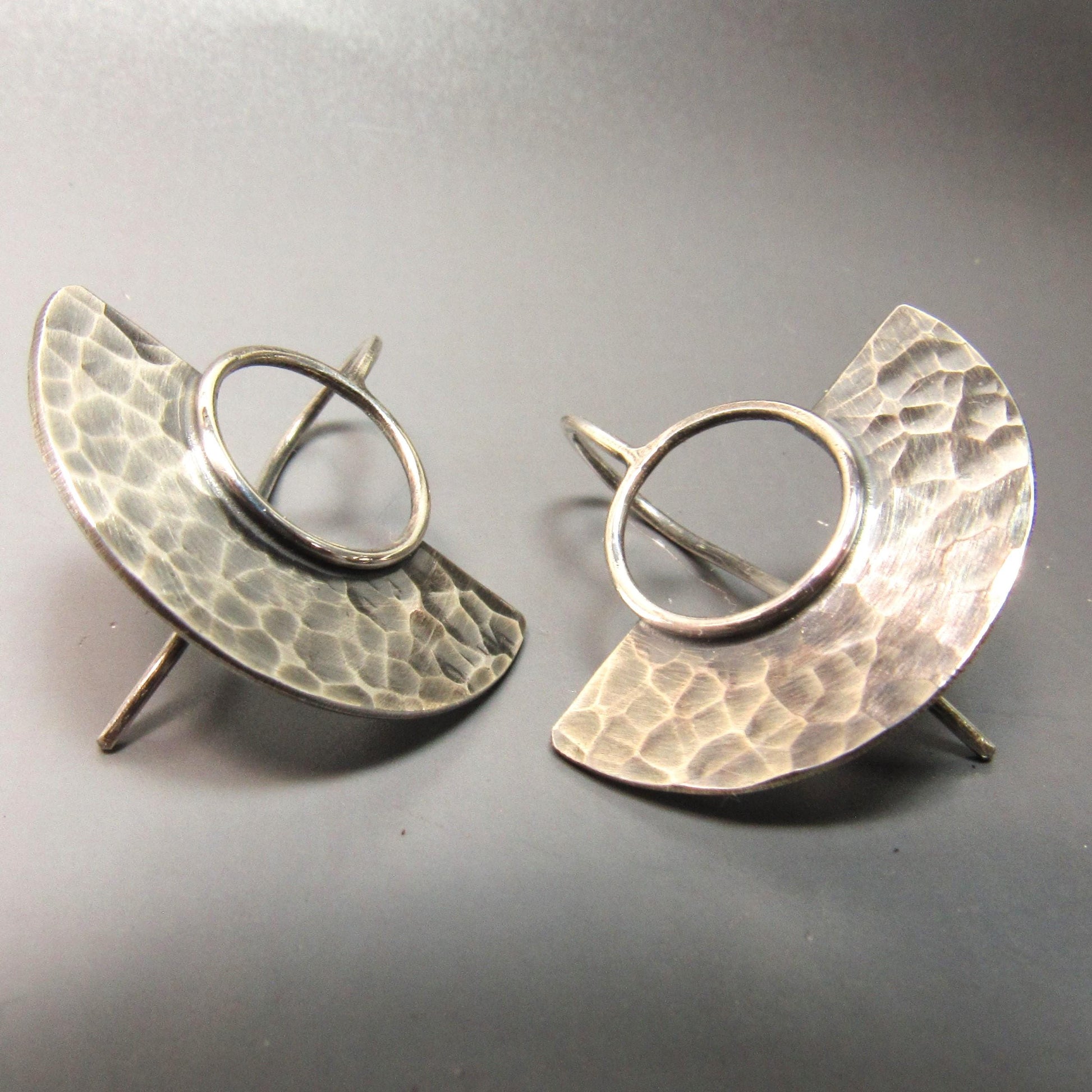 Pair of silver earrings with textured half-circle design on a gray background