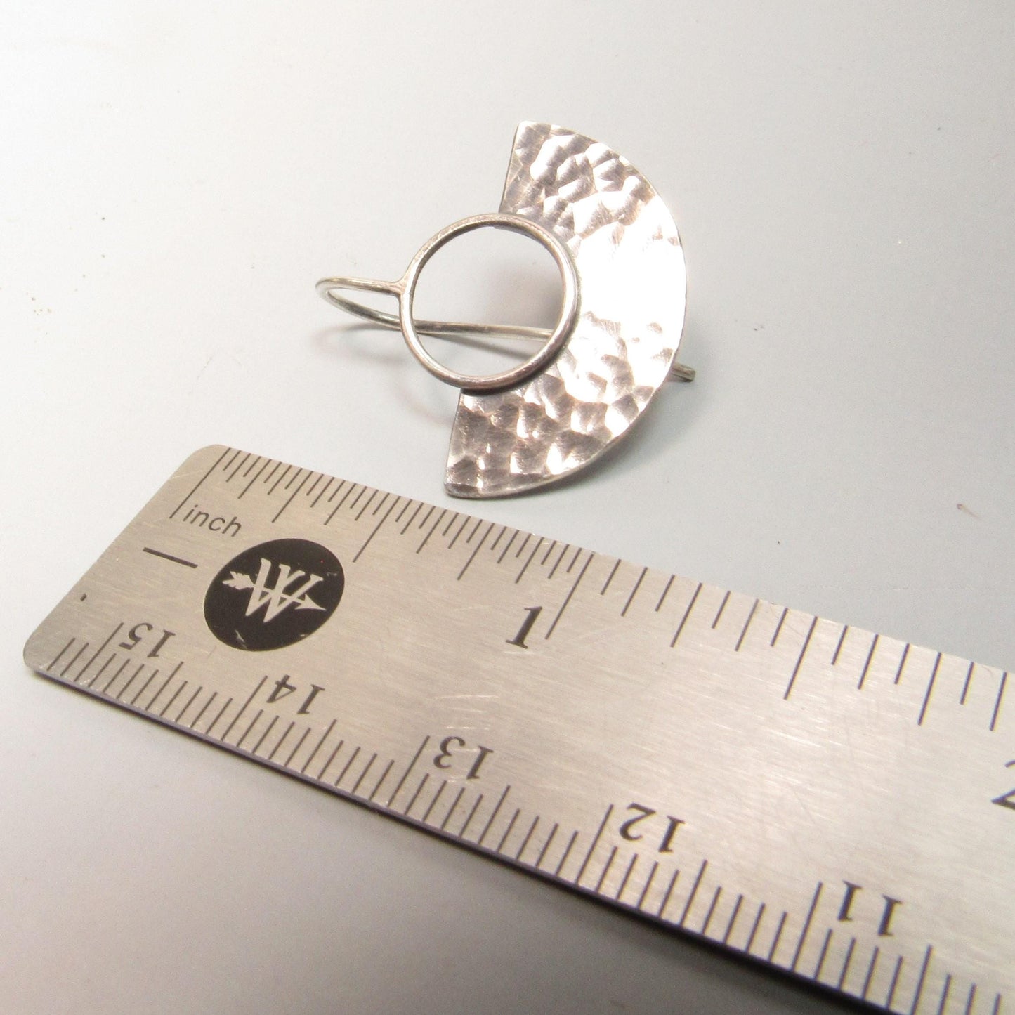 Silver fan earrings with hammer texture on a ruler for scale on a white background.