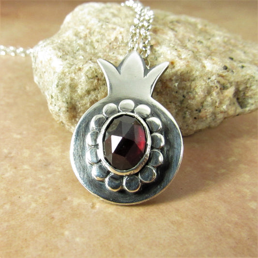 Argentium Silver pomegranate pendant with a red garnet on a stone background.
