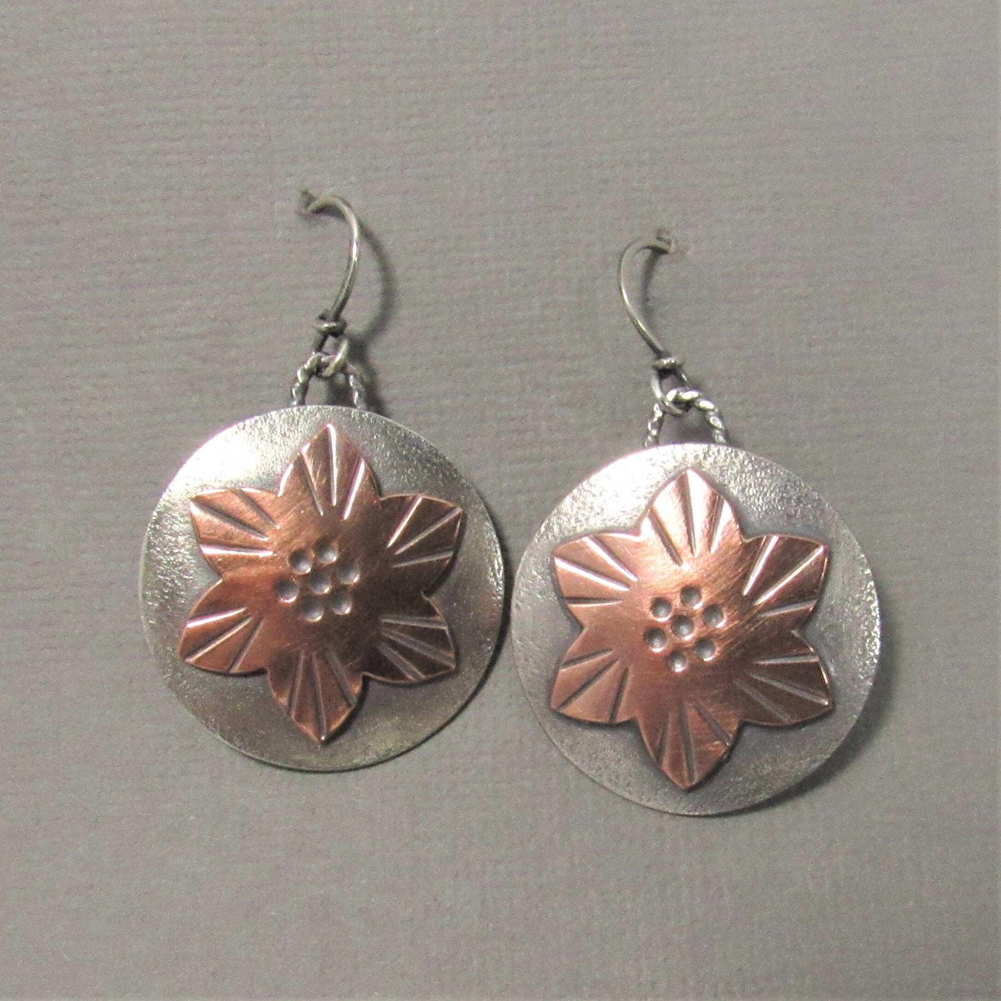 Mixed metal flower earrings handcrafted from copper and Argentium silver, lightly oxidized for depth and texture. On grey background.