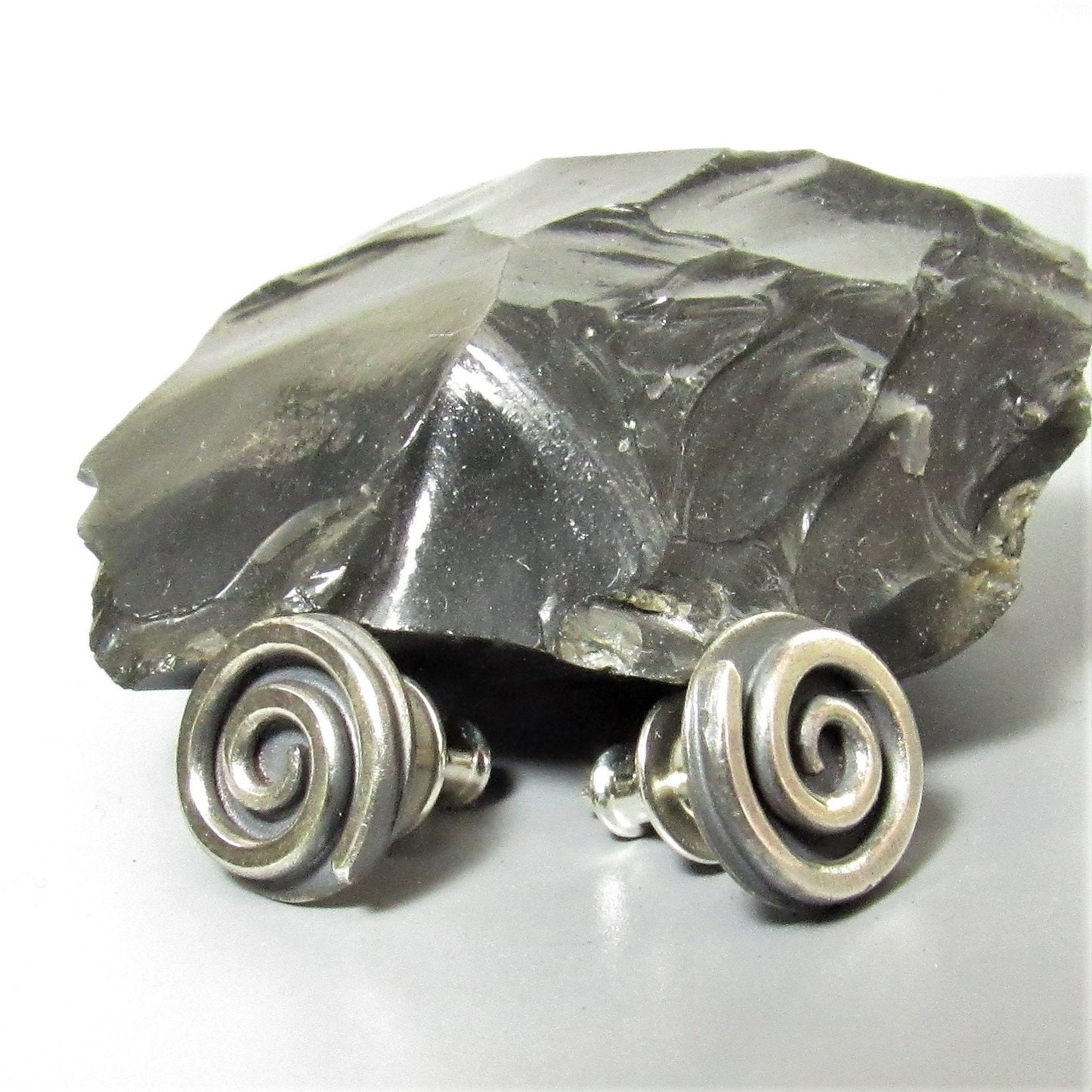 Argentium silver spiral earrings with a black  rock on a light background.