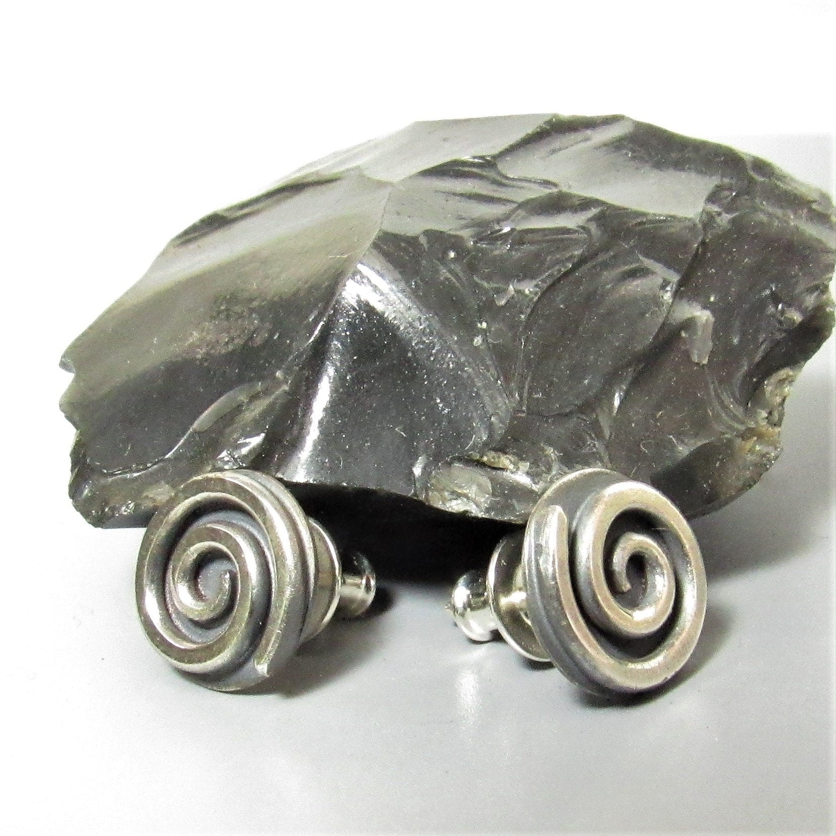 Argentium silver spiral earrings with a black  rock on a light background.