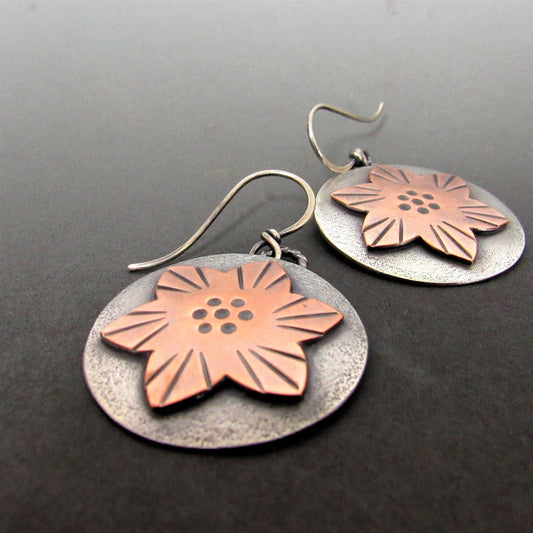 Handcrafted copper and Argentium sterling silver star flower earrings with oxidized finish, artisan made by Mocahete. Photo on dark background.