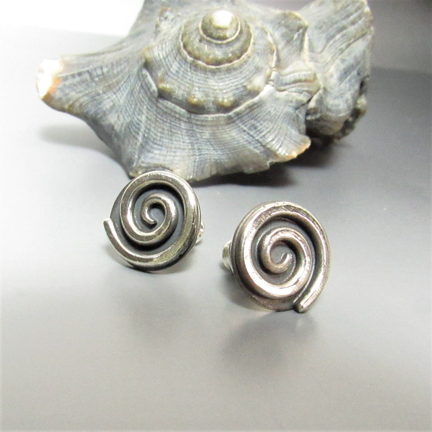 Mocahete handcrafted silver spiral earrings with a shell on a light gray background.