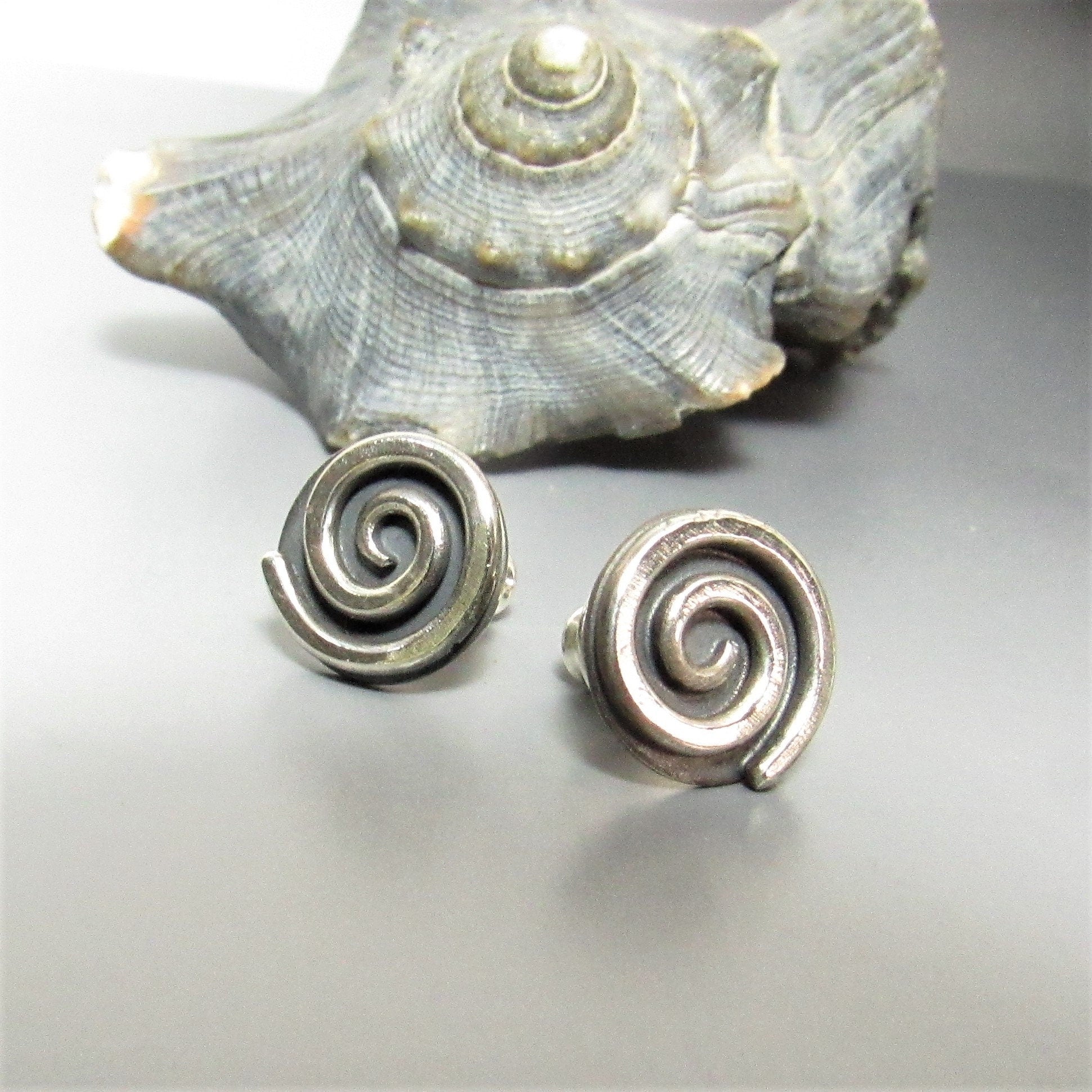 Mocahete handcrafted silver spiral earrings with a shell on a light gray background.
