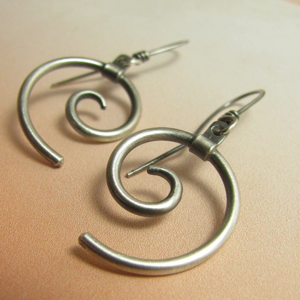 Satiny smooth handcrafted SS spiral earrings on orange background.