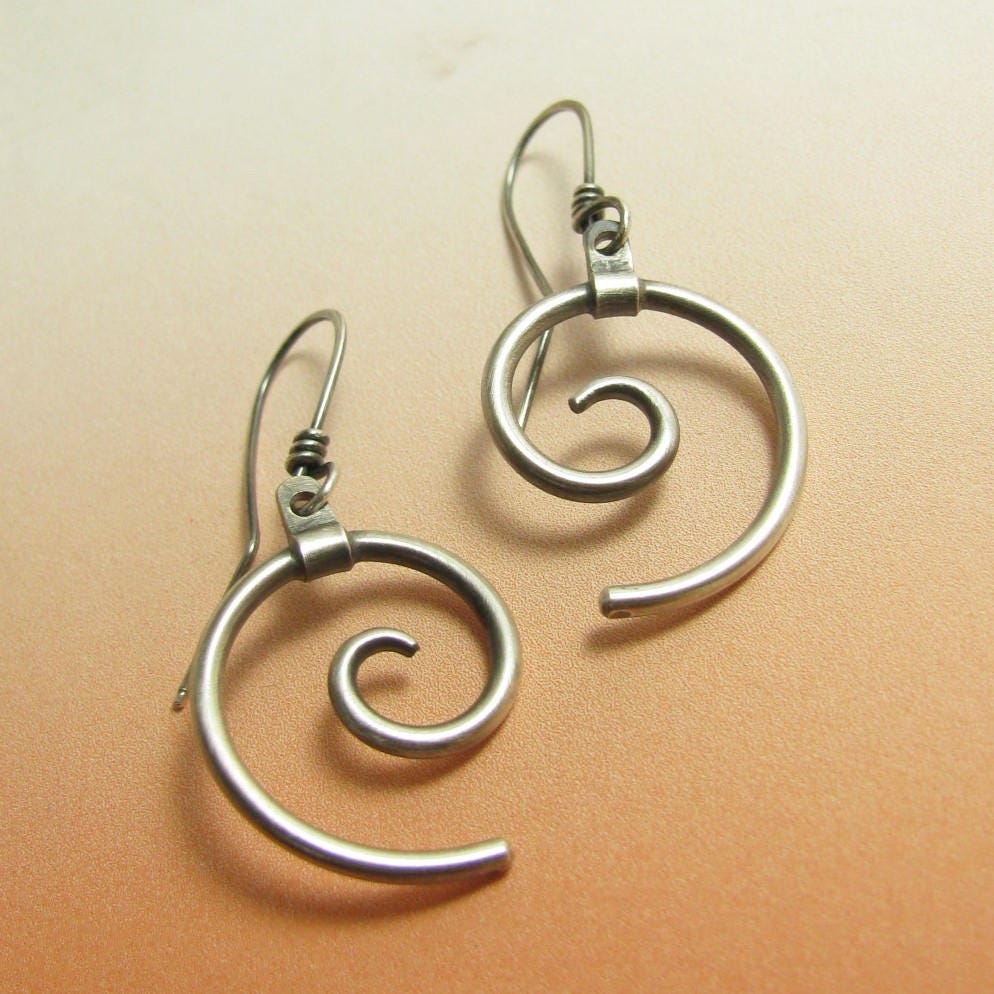Sleek silver spiral earrings on orange background.