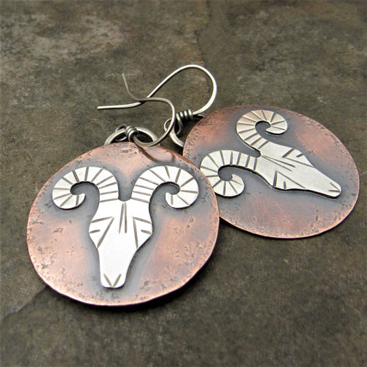 Mixed metal rams head earrings on dark background.