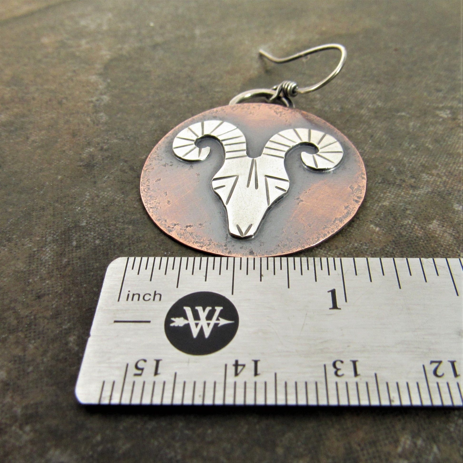 Rams head earrings on dark background with ruler.