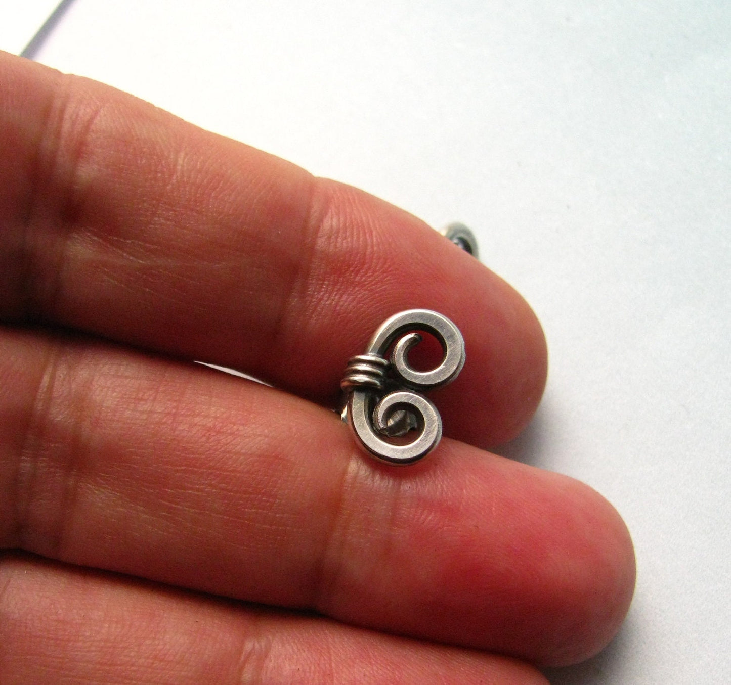 Sterling silver spiral earrings held between fingers on white background.