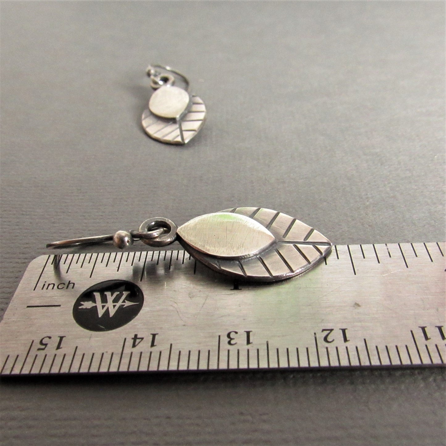 SS leaf earrings against ruler on grey background.