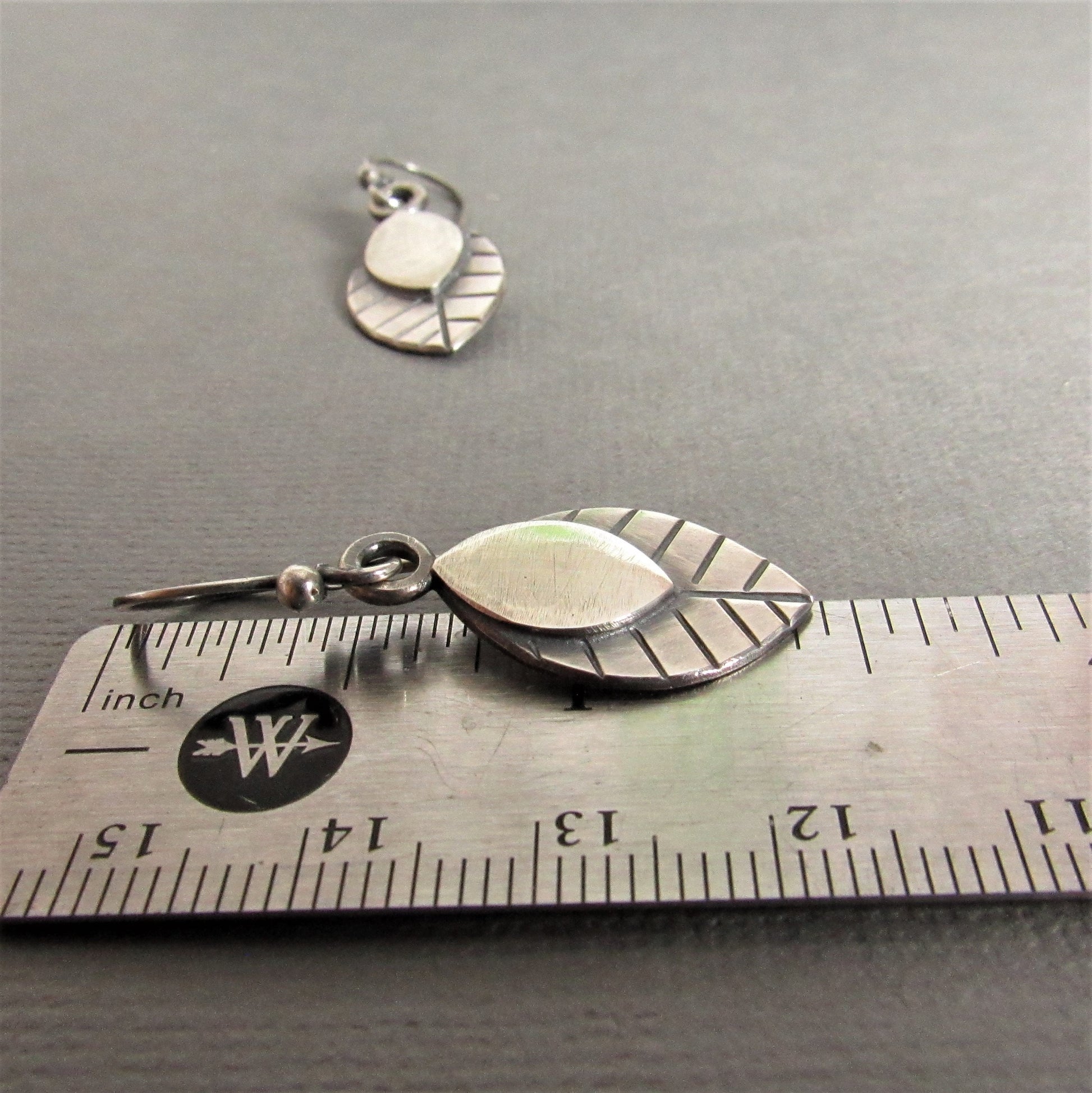 SS leaf earrings against ruler on grey background.