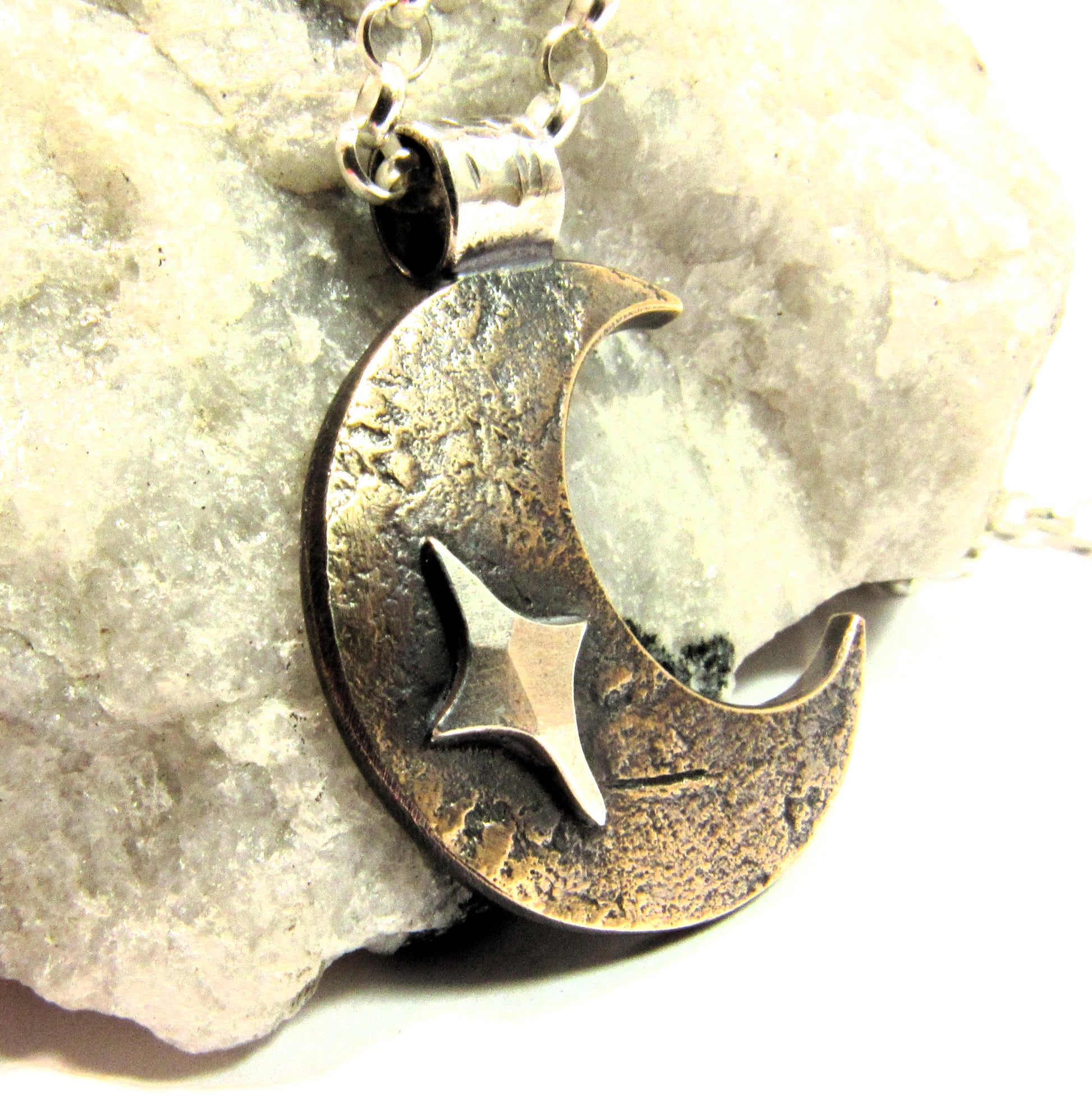 Copper and silver pendant with star and crescent moon on sterling silver chain, photo with rock background.