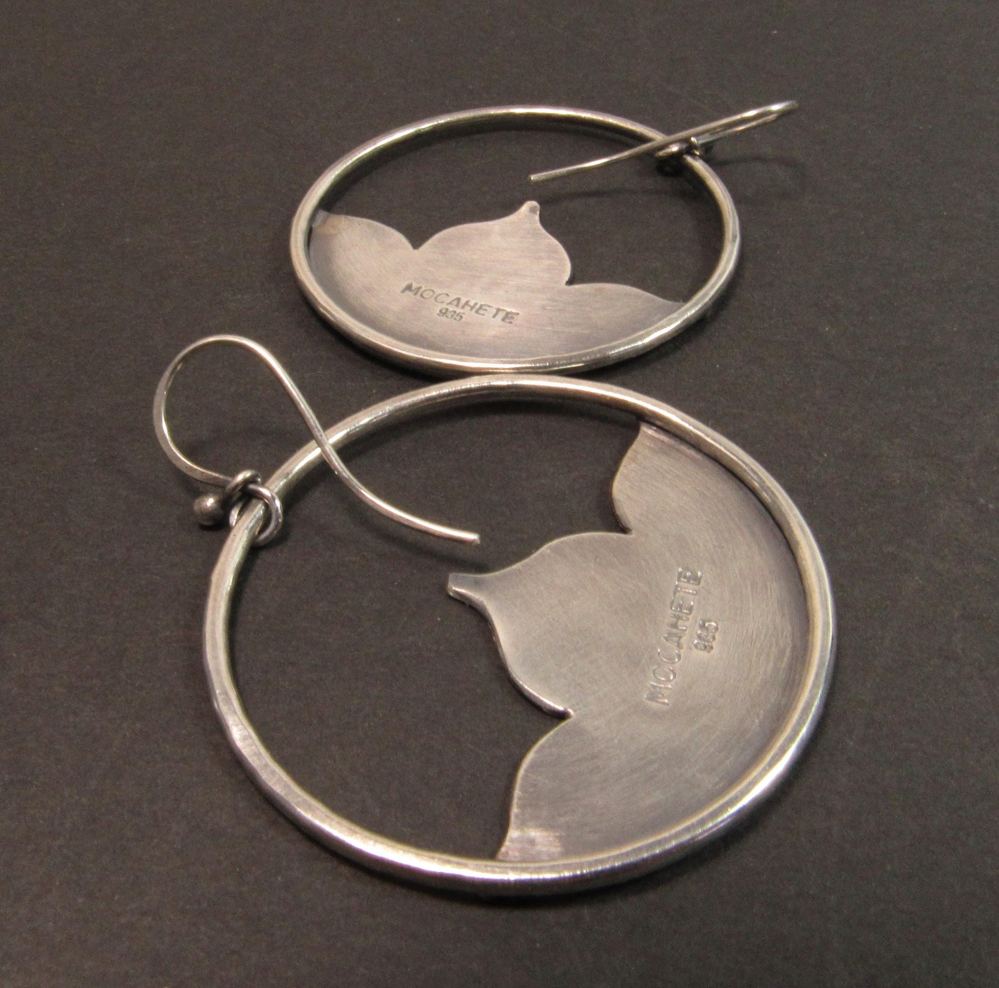 Backside of SS lotus earings showing makers mark on dark backgroumd.