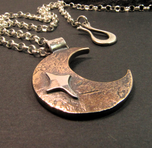 Rustic unisex crescent moon pendant necklace in copper and silver on dark background.