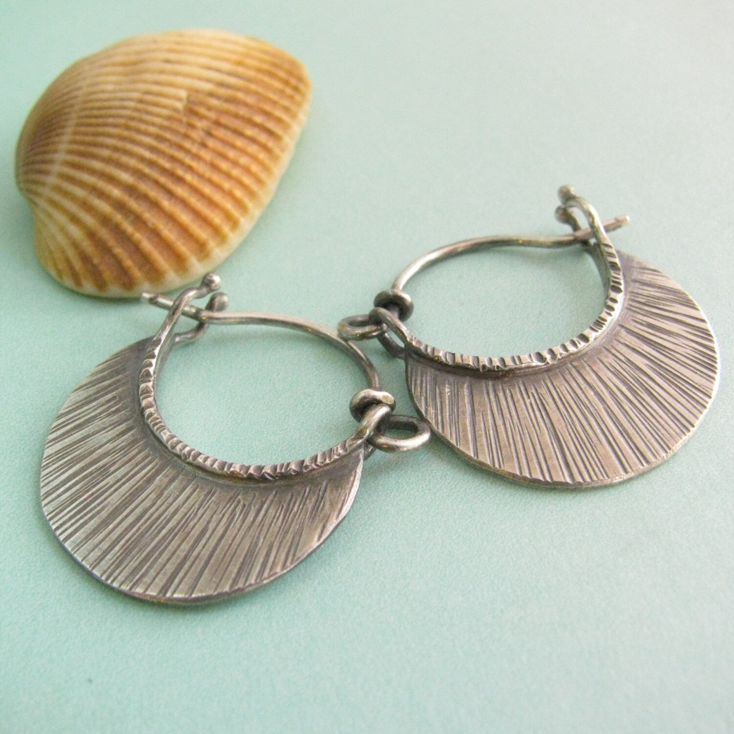 Little sterling hoop earrings with texture on blue background with shell.