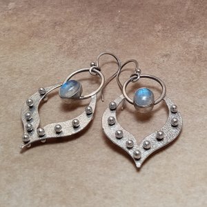 Argentium silver and moonstone earrings with tribal influence displayed on light brown background.