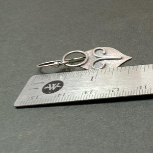 Argentium silver dangle earrings in a mask shape with wire embellishment. Displayed against ruler on grey background.