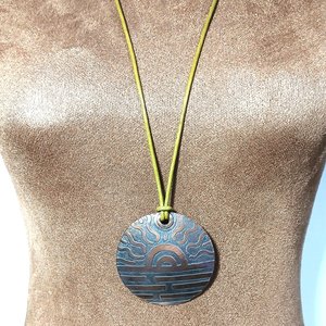 Large copper disk pendant hung on leather cord displayed on mannequin.