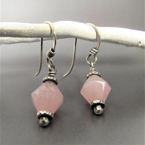 Pink quartz and sterling silver drop earrings dangling from white branch against gray background.
