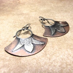 Mixed metal dangle earrings with copper and silver, floral detail, displayed against sand color background.