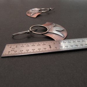 Fan shape earrings in copper and silver displayed against ruler to show length. Apx. 1.5" long. Black background.