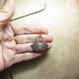 Mixed metal dangle style earrings in a fan shape with floral detail by Mocahete. Displayed in hand against sand color background.