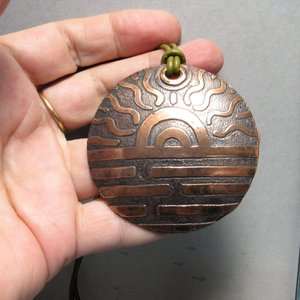 Large etched copper sun pendant displayed in hand.
