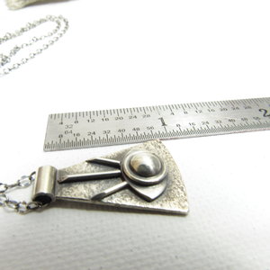 Eye of providence necklace displayed against ruler to show size.