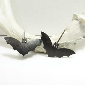  A  pair of bat earrings with oxidized copper body, sterling silver eyes and ear wires. Displayed on white antler and background.
