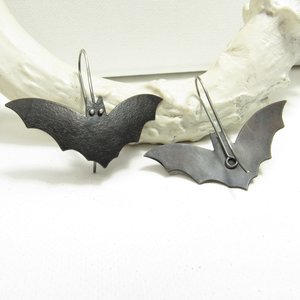 Bat earrings showing reverse side of one.  Displayed on white antler and background.