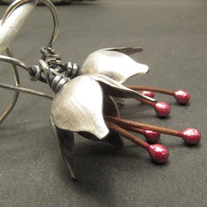 Argentium silver and pure reddened copper winter bell flower earrings. Displayed hanging on white branch on grey background.