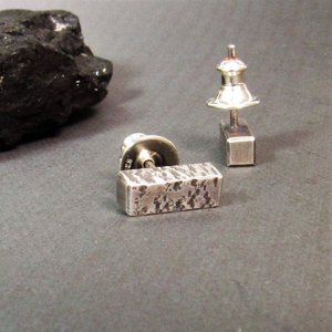 Unisex sterling silver earrings with a textured rectangular design. The earrings have  silver post backs included. Displayed against rock with grey background.
