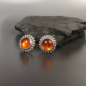 Amber and sterling silver stud earrings displayed against black rock on grey background.